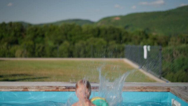 Happy kid having fun when jumping to swimming pool with inflatable armbands. Summer outdoor water activity for kids.