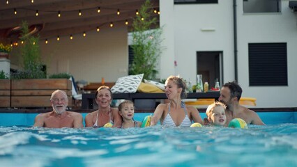 Multi generation family having fun and enjoying swimming in backyard pool during summer holiday.