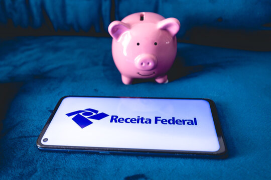 Receita Federal - RFB. Um telefone celular com a logo da Receita Federal do Brasil e um cofrinho sobre um sof&aacute; azul. Imposto de renda, darf, declara&ccedil;&atilde;o anual.