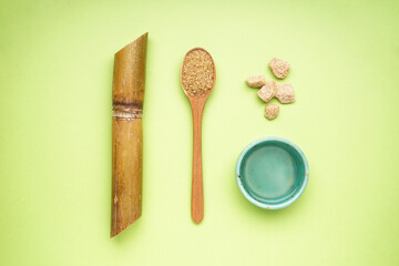 Sugar cane and wooden spoon on green background, top view.