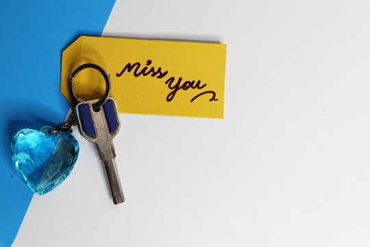 Miss you hand written in yellow paper tag with blue heart key chain in white background