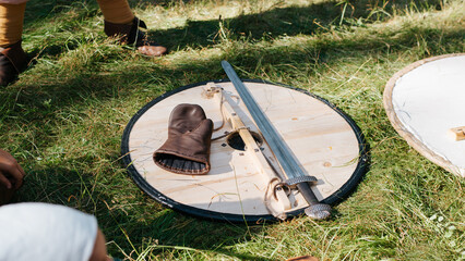 Armament of a viking medieval warrior sword, wooden shield and glove lying on the grass outdoors