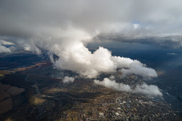 Aerial view from airplane window at high altitude of distant city covered with white puffy cumulus clouds