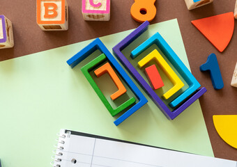 Wooden kids toys on colourful paper. Educational toys, blocks, pyramid, pencils, numbers, rainbow. Toys for kindergarten, preschool or daycare. Copy space for text. Top view. Back to school background