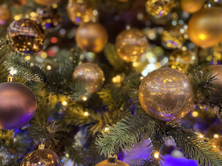 Fototapeta na wymiar Green branches of a fluffy Christmas festive New Year tree with toys in balls and bright glowing light bulbs and garlands, background.