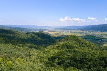 Fototapeta premium Aerial view of mountain hills covered with dense green lush woods on bright summer day