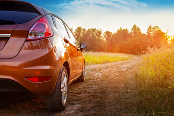 Car in the field at sunset. Close-up of an orange car on a country road, car travel at sunset background, travel from nature by car, journey, summer and lifestyle.