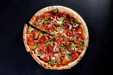 Vegan pizza with tomato sauce, cherry tomatoes, mushrooms, broccoli, red onion on black background. View from above