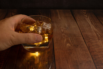  liquor glasses of whiskey, rum, etc, illuminated liquor from inside the glass tumbler with ice cubes wooden table with glass reflection, text space