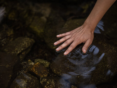 Close-up image of an Indigenous person touching a stream with their hands 