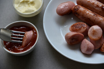 Fried meat sausage with sauces on a gray background. Meat breakfast with sausage and sauces on a plate with a fork.