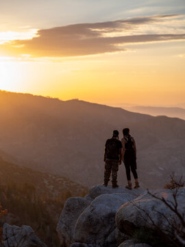 Vertical image of young native friends standing at the edge of a cliff watching the sun set