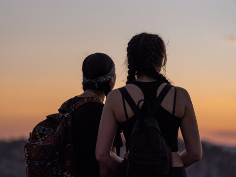 Horizontal image of two native friends looking out towards sunset