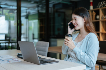 Young business women working on laptop and talking on a phone calling with happy and smile face on...