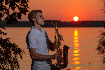 A young guy plays the saxophone in the evening at sunset