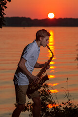 A young guy plays the saxophone in the evening at sunset