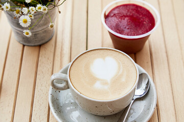  Cappuccino in a white ceramic cup and pick up raspberry jam dessert in a disposable cup, a snack on the cafe terrace. Flat lay close up of food