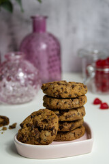 Chocolate crispy cookies stacked in a stack on a ceramic plate close-up against the background of pink vases and heart-shaped marmalades