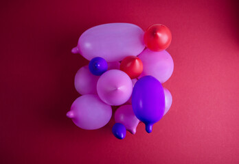 Pink, purple and red balloons of different shapes and sizes are laid out on a red background in the shape of a square.