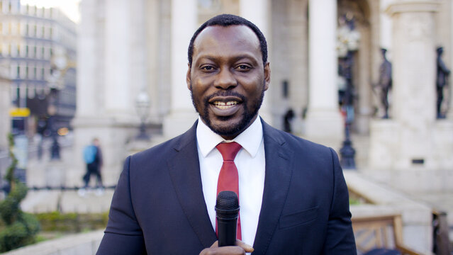 Portrait of black male news reporter holding a microphone to camera