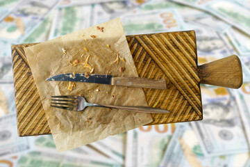 dirty fork and dirty knife after eating on a wooden base on a blurred background of one hundred dollar bills