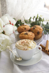 A cup of coffee with whipped cream next to a plate on which there are muffins with chocolate 