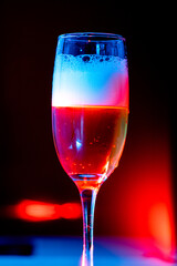 glass of beer with foam on with red light. water drops on the glass. black background 