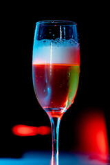 glass of champagne with foam on with red light. water drops on the glass. black background 