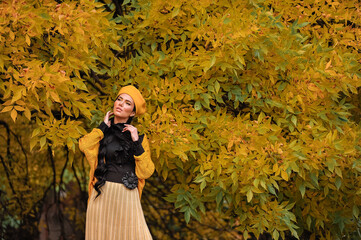 a beautiful brunette with makeup in a yellow beret and yellow jacket walks in the park in autumn.