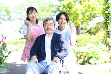 屋外で車椅子に乗る高齢者と男女の介護士
