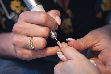 professional manicure with an electric drill at the client's home, grinding and polishing of nails during a home visit. closeup photo.