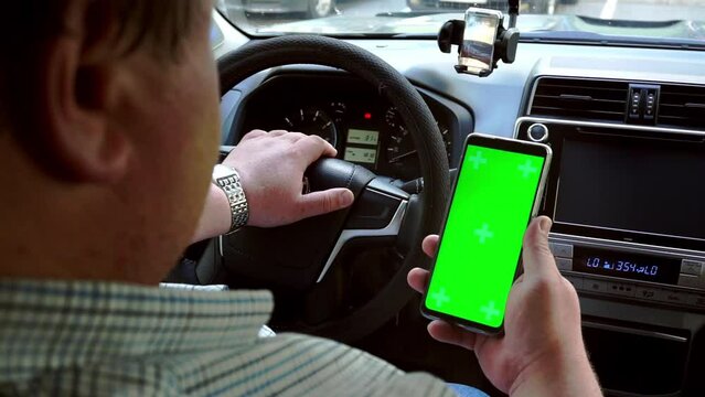 Man hold smartphone with green screen with Car dashboard background. Open conceptual for technology stuff. Chroma key.