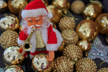 little doll of Santa Claus with saxophone on front with golden Shimmering balls in background. Christmas decoration