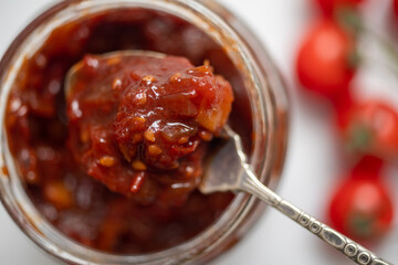 Homemade spicy tomato chutney on a spoon from a jar. - obrazy, fototapety, plakaty