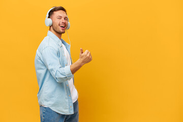 Dancing happy tanned handsome man in blue basic t-shirt headphones show thumb up gesture Like posing isolated on orange yellow studio background. Copy space Banner Mockup. Time to relax concept