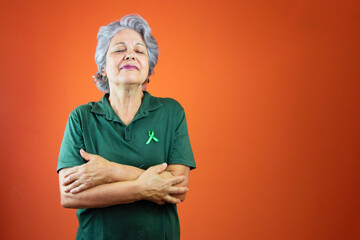 World mental health day - Mature Woman With Gray Hair, green ribbon and shirt isolated on orange.