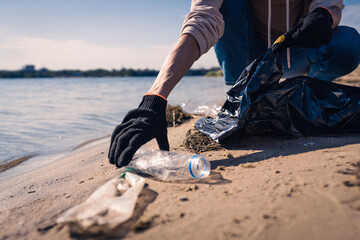 Woman cleaning lake shore from garbage putting trash in bag. Environmental problems concept.