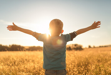 It's a beautiful life! Child standing in a field at sunset having feelings of freedom, hope, and...