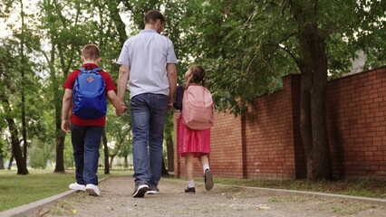 happy family. father holding hands children school. little kids school bags go school holding dad...