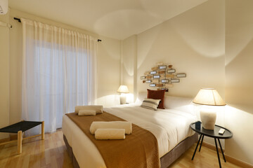 Bedroom decorated in soft tones, twin lamps, white curtains and clean rolled towels