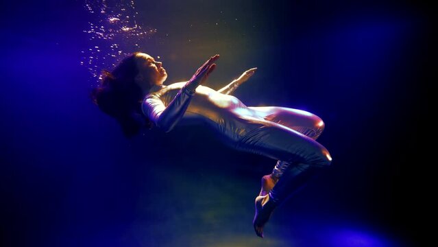woman in shiny metallic suit is diving and drowning in mysterious dark depth, unreal cosmic