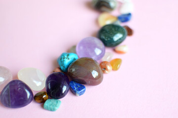 Semi-precious stones of different colors on a pink background. Amethyst, rose quartz, agate, apatite, aventurine, olivine, turquoise, aquamarine, rock crystal on a pink background. Selective focus.