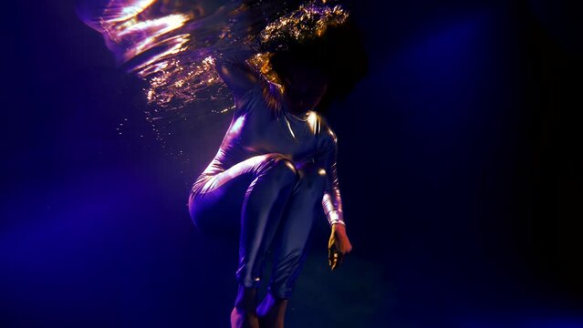 fantastic underwater shot with woman in shiny metallic suit floating in dark blue water