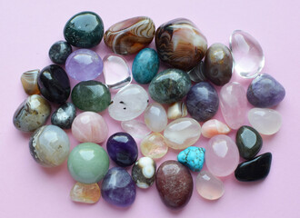 Semi-precious stones of different colors. Amethyst and amethyst druse crystals, rose quartz, agate, apatite, aventurine, olivine, turquoise, aquamarine, rock crystal on a pink background.