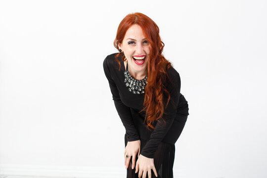 young red-haired girl in a black dress. Redhead young woman. White background. Red lips. Studio photo. Happy elegant lady