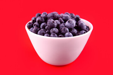 Beautiful fresh blueberries in a white bowl on a red background.Vegan and vegetarian concept. Summer healthy food.