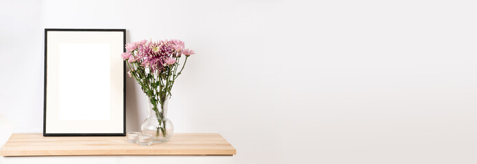 A mock-up of a black photo frame on wooden table, a transparent vase with pink summer flowers,...