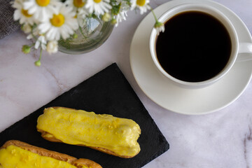 A white cup with black coffee and lemon eclairs on the table. Confectionery for sweet tooth.