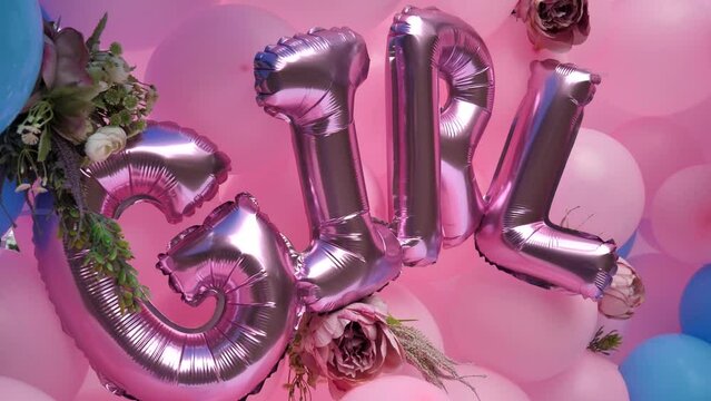 Letters from pink helium balloons forming the word Girl during a gender reveal party against the background of colored balloons
