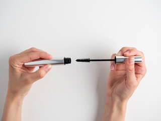 Women's hands hold the mascara open on a white background. A brush for applying mascara. The concept of cosmetics